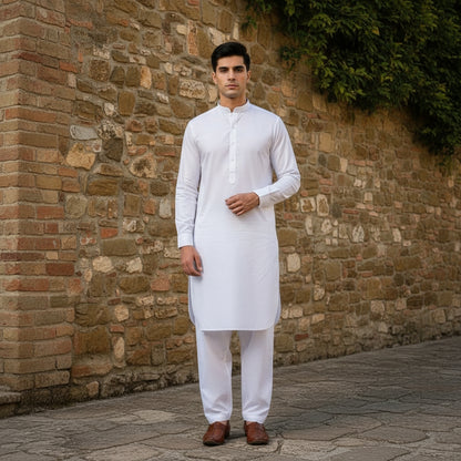 Man wearing a white pasha cotton kurta and pants standing against a stone wall.