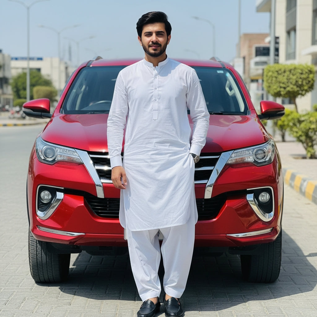 Man in white pasha cotton traditional outfit standing in front of a red car on a street.